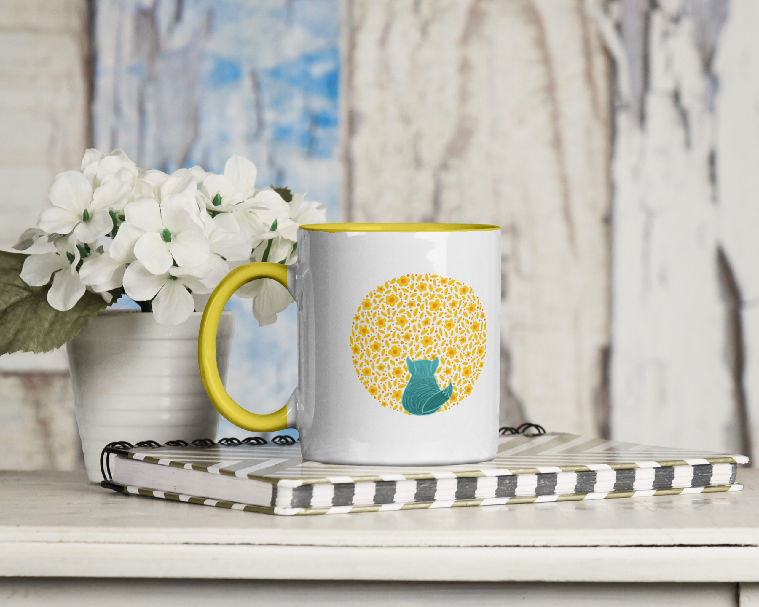 A white mug with yellow handle and yellow interior, featuring a teal fox outlined against yellow flowers. Available to purchase from Little Bird Creative's online shop